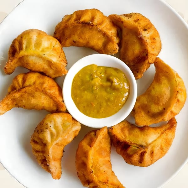 A plate of golden-brown fried momos arranged around a small bowl of green dipping sauce.
