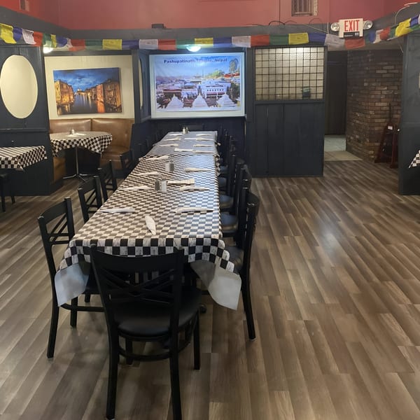 Long dining table with checkered tablecloths and black chairs in a restaurant with cultural decor.