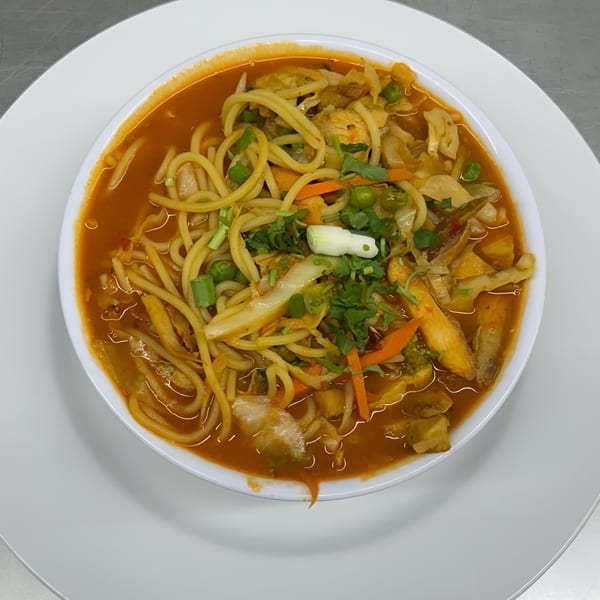 A bowl of Indian thukpa with noodles, vegetables, and a rich orange broth.