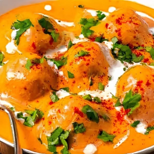 Indian chicken curry with a creamy orange sauce, garnished with fresh cilantro and red spices.