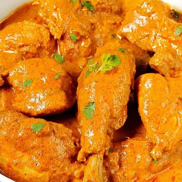 Close-up of Indian chicken curry with rich orange sauce and green herb garnish.