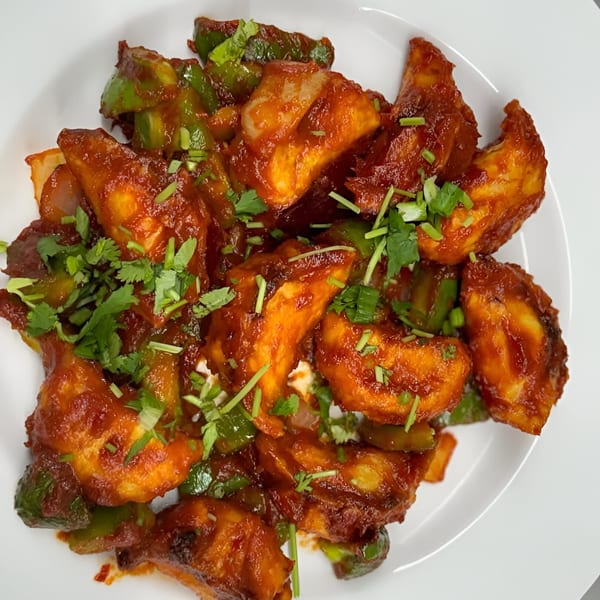 Chili Paneer, an Indian dish, with bell peppers and cilantro on a white plate.
