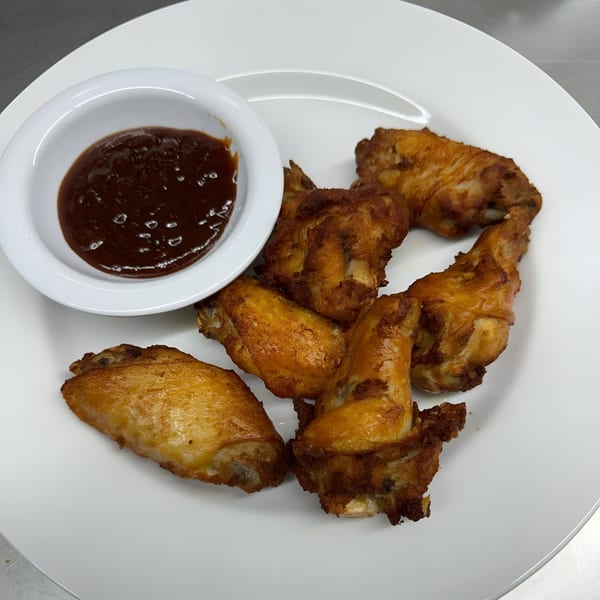 Crispy fried chicken wings with a side of dark dipping sauce on a white plate at MOMO HOUSE AND GRILL.