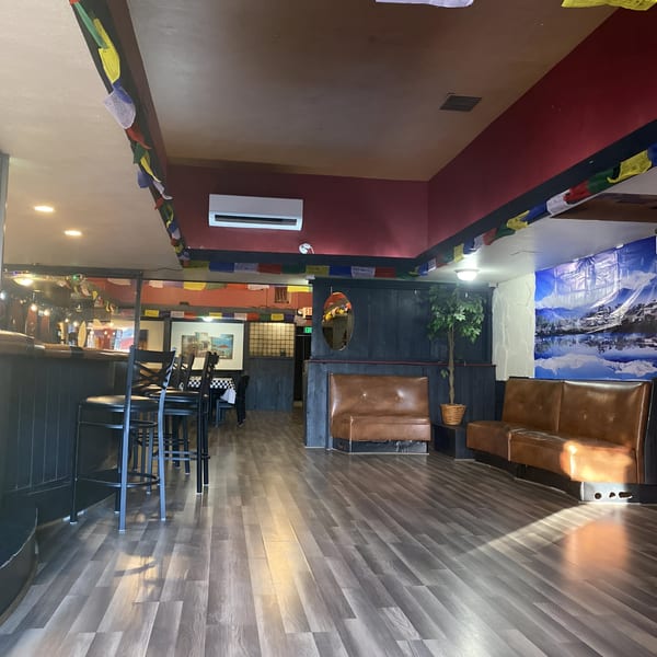 Empty MOMO HOUSE AND GRILL dining room with prayer flags, brown booths, and a bar area.