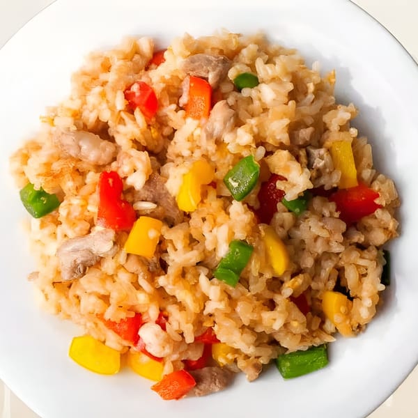 Close-up of Indian fried rice with chicken, red, yellow, and green bell peppers on a white plate.
