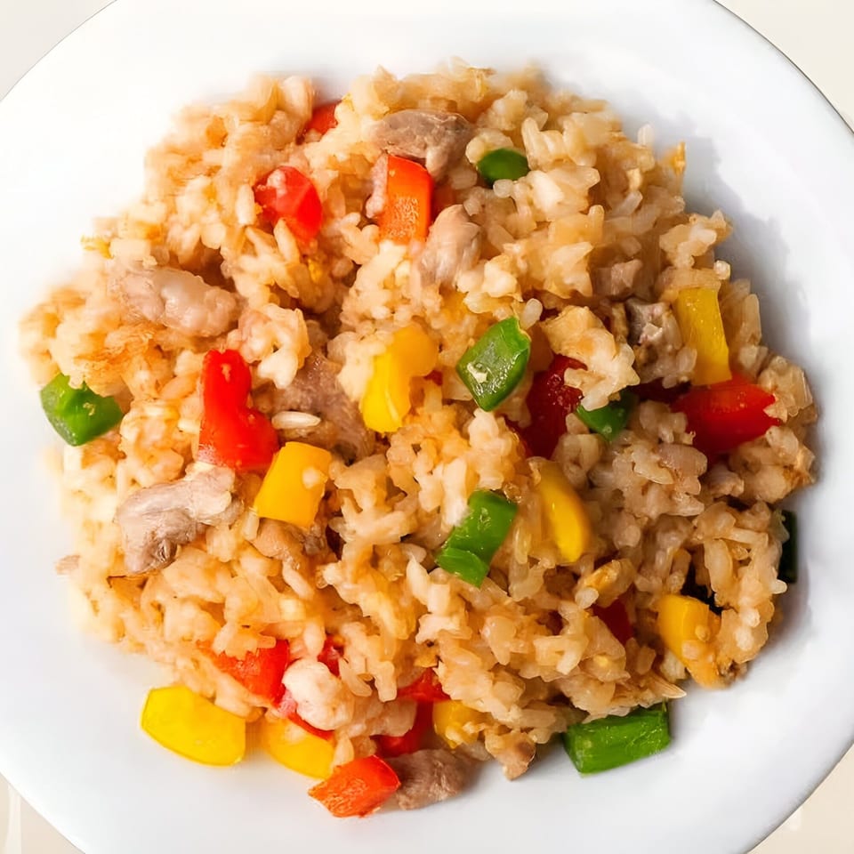 Close-up of Indian fried rice with chicken, red, yellow, and green bell peppers on a white plate.